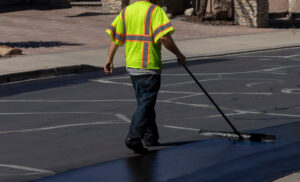 Worker using a sealcoating brush during asphalt resurfacing proj Worker using a sealcoating brush during asphalt resurfacing project